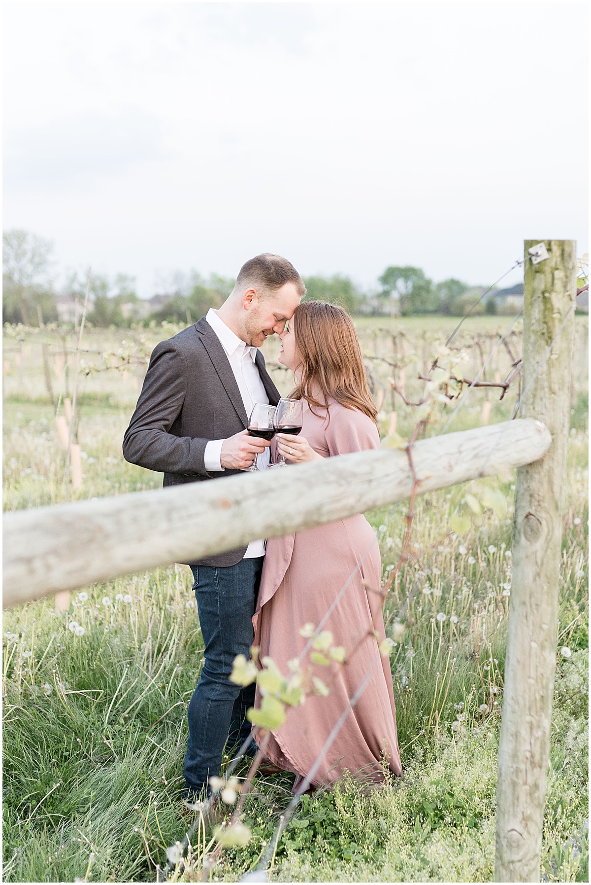 Couple drinking wine in winery fields during photos by Indianapolis wedding photographer Victoria Rayburn Photography