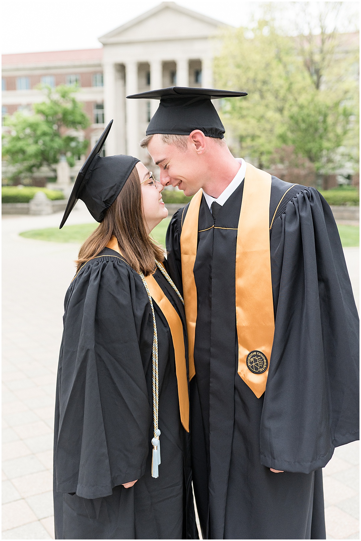 Couple in cap and gown enjoying engagement and graduation photos at Purdue University in front of Purdue Arch