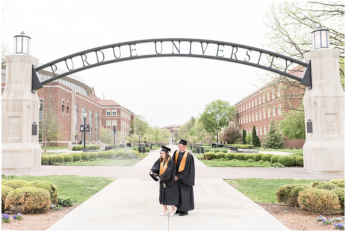Couple in cap and gown enjoying engagement and graduation photos at Purdue University in front of Purdue Arch