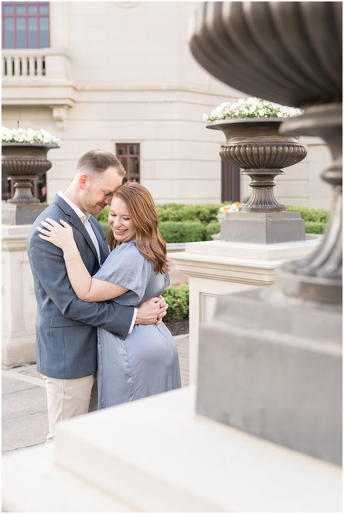 Couple hug next to plants during engagement photos at The Palladium in Carmel, Indiana