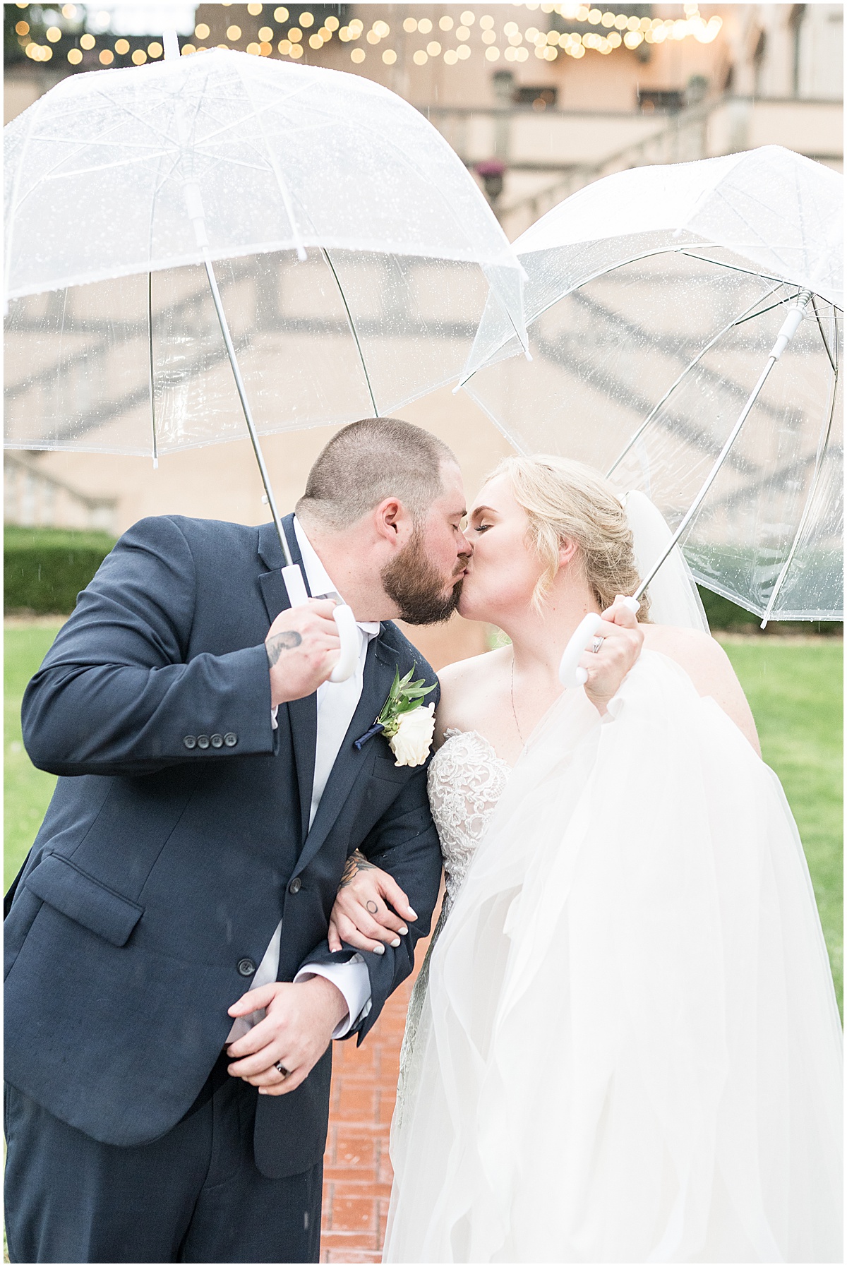 Bride and groom kiss under umbrellas at rainy Fowler House Mansion wedding