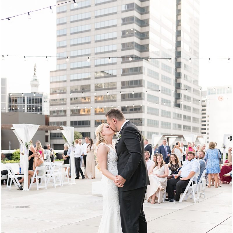 Bride and groom kiss after first dance on rooftop in downtown Indianapolis