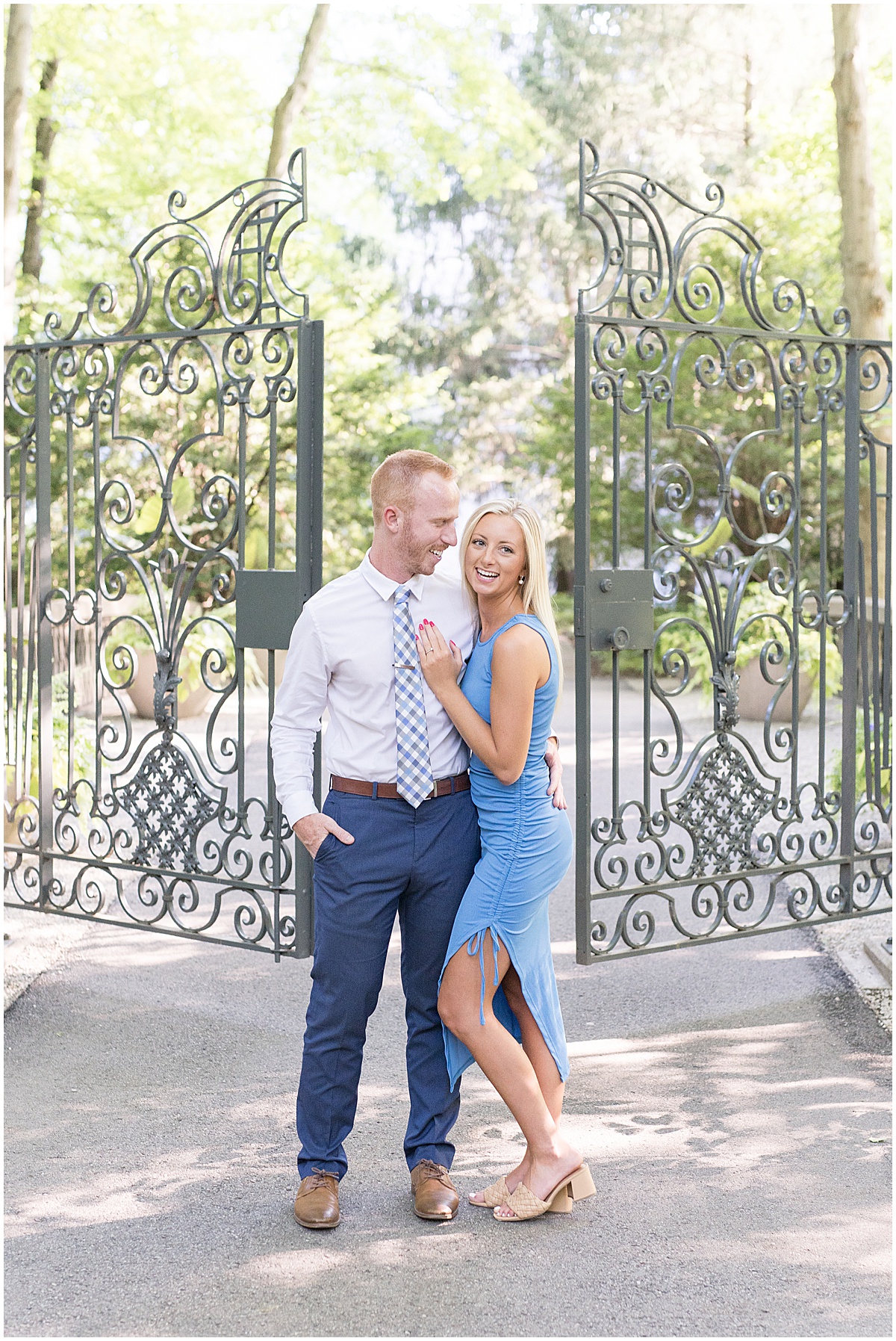 Couple laugh in front of gate at summer engagement photos at Newfields in Indianapolis
