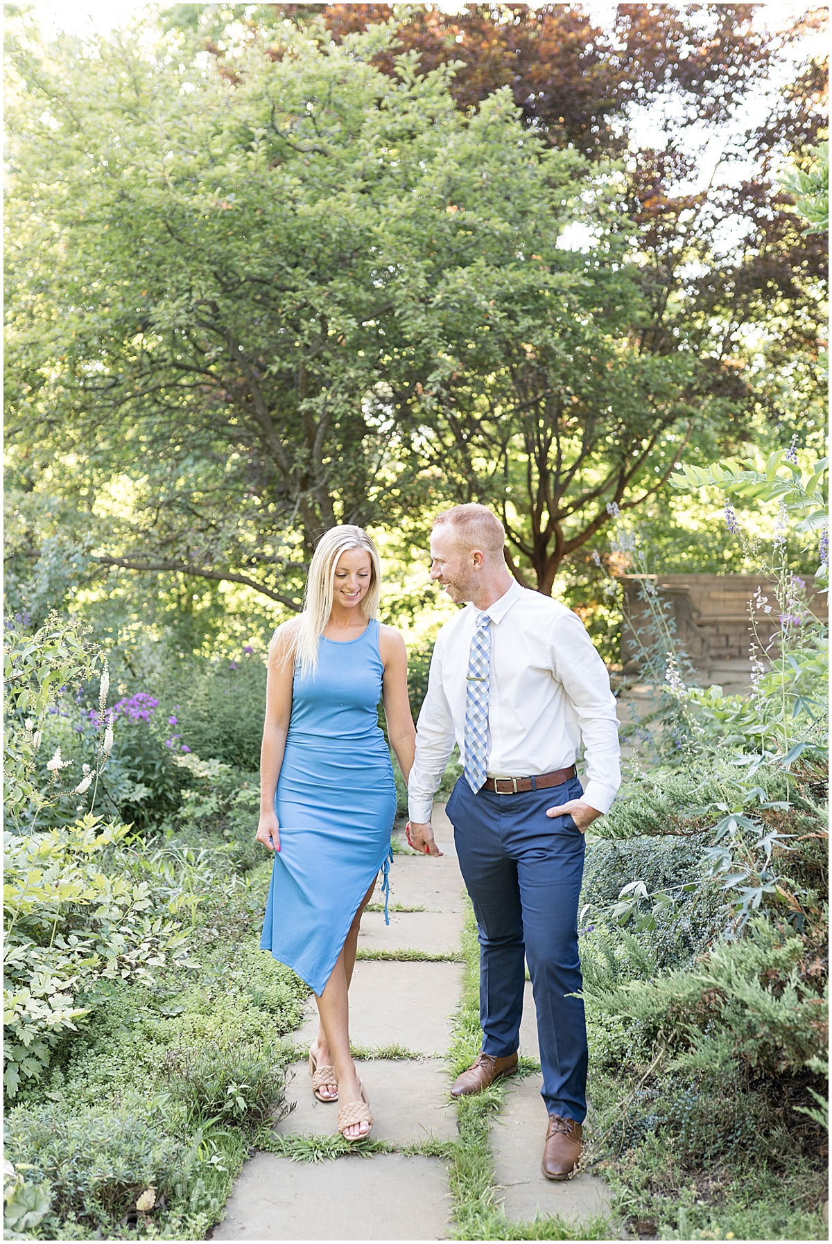 Couple holds hands on path at summer engagement photos at Newfields in Indianapolis