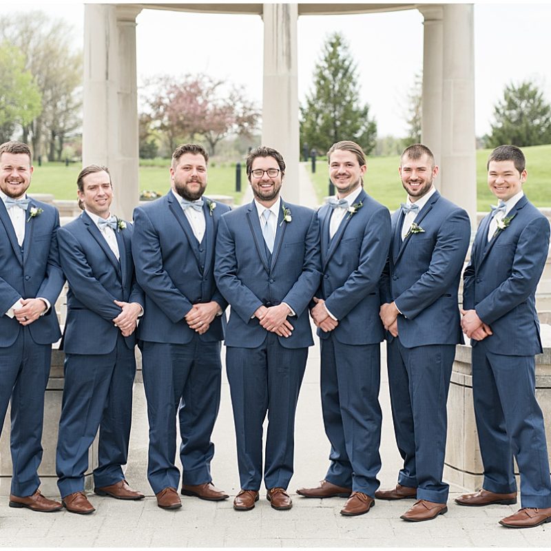 Groomsmen stand by fountain during wedding photos at Coxhall Gardens