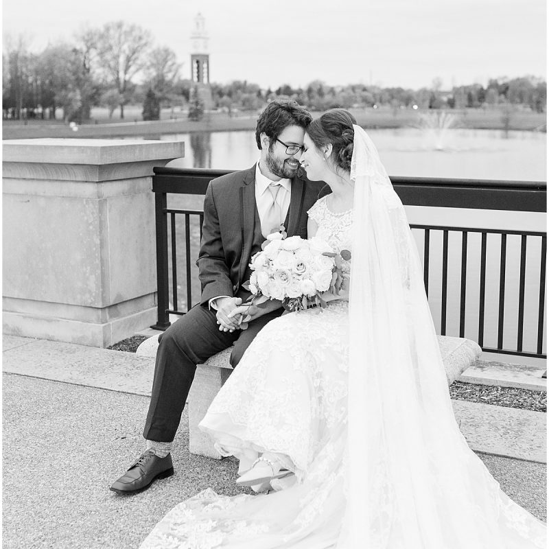 Bride and groom sit on bench during wedding photos at Coxhall Gardens