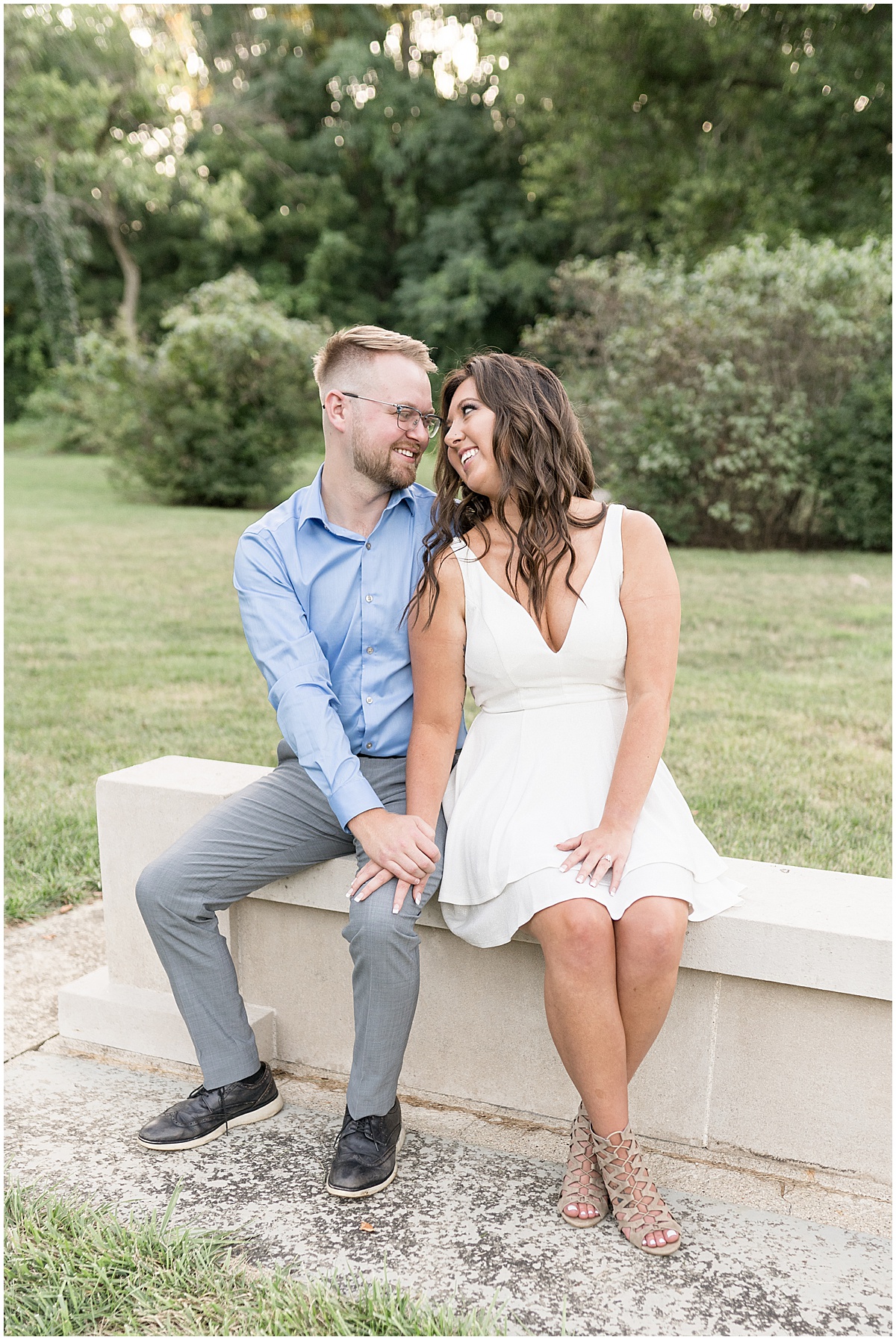 Couple sitting on wall during summer engagement photos at Holcomb Gardens in Indianapolis