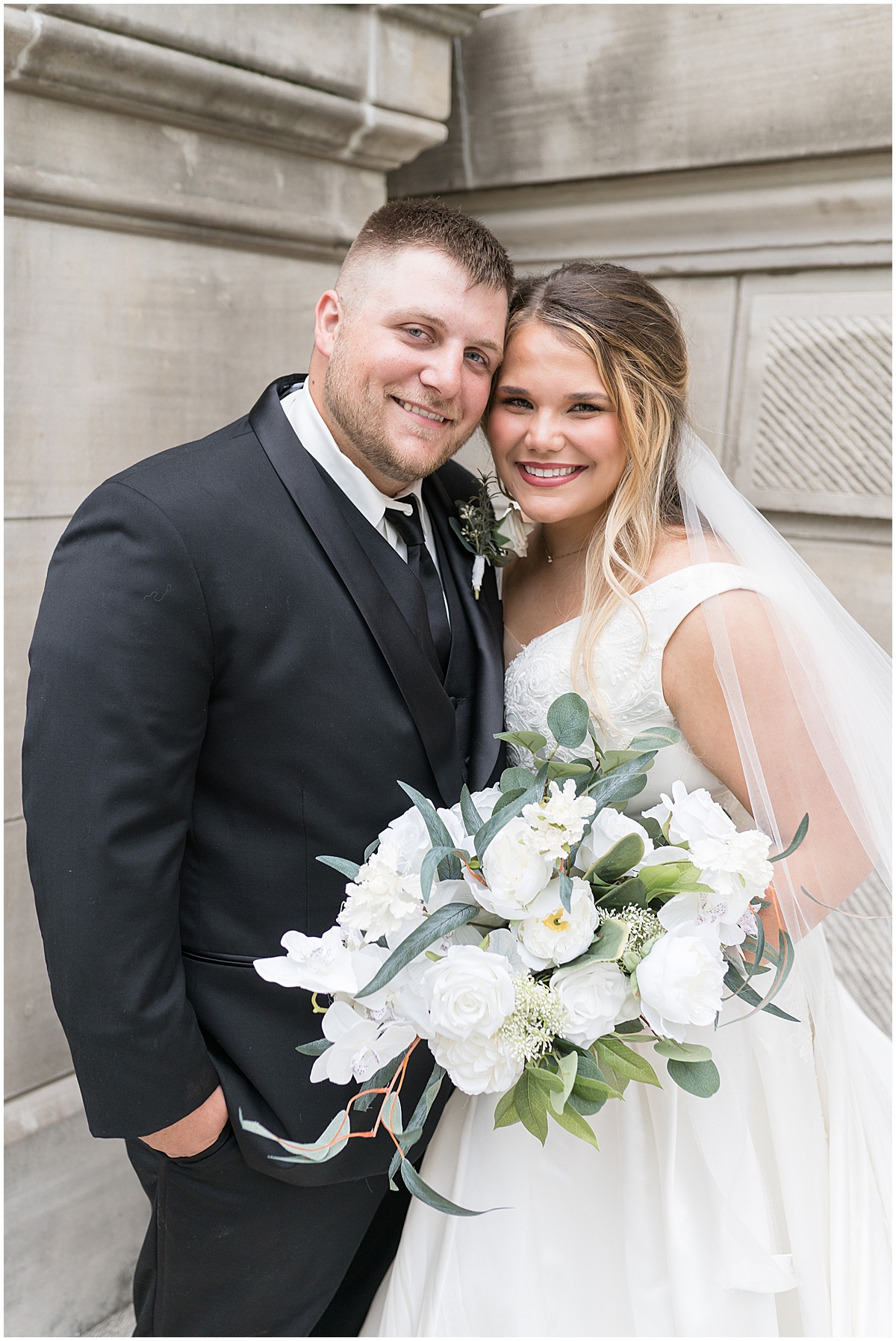 Bride and groom pose by stonework during wedding photos at Hamilton County Courthouse in downtown Noblesville, Indiana 
