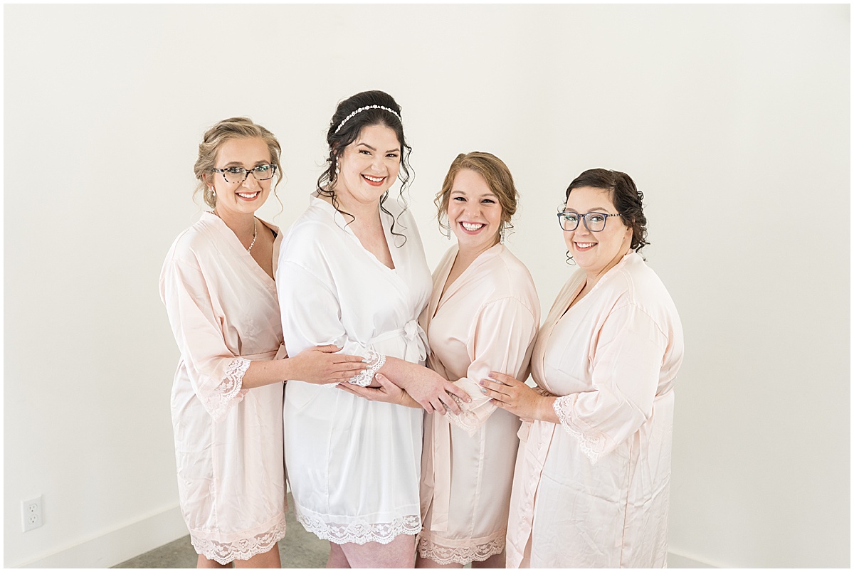 Bride and bridesmaids in light pink robes before pastel wedding at New Journey Farms in Lafayette, Indiana