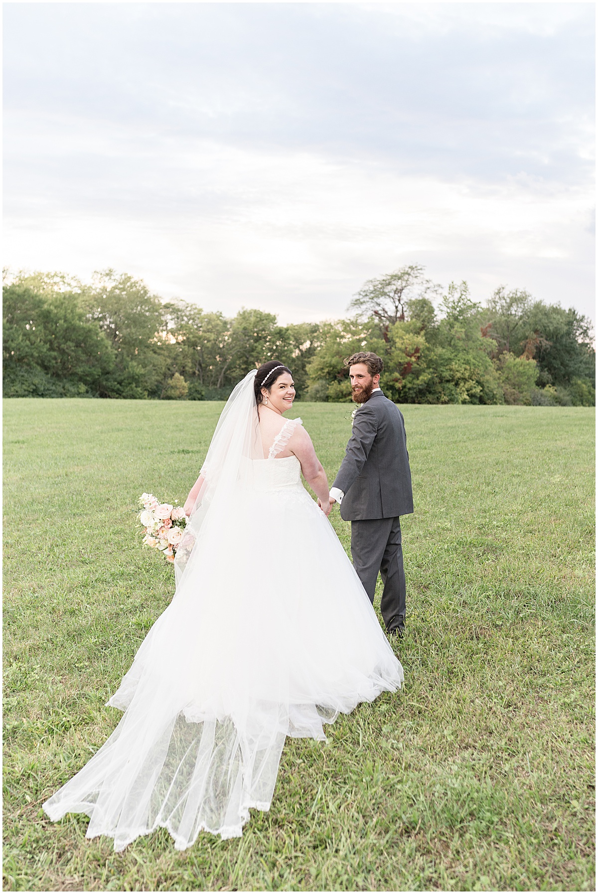 Bride and groom walking in field after pastel wedding at New Journey Farms in Lafayette, Indiana