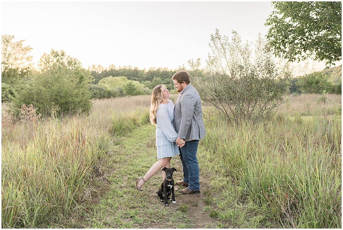 Couple with dog walk on path during summer engagement photos at Fairfield Lakes Park