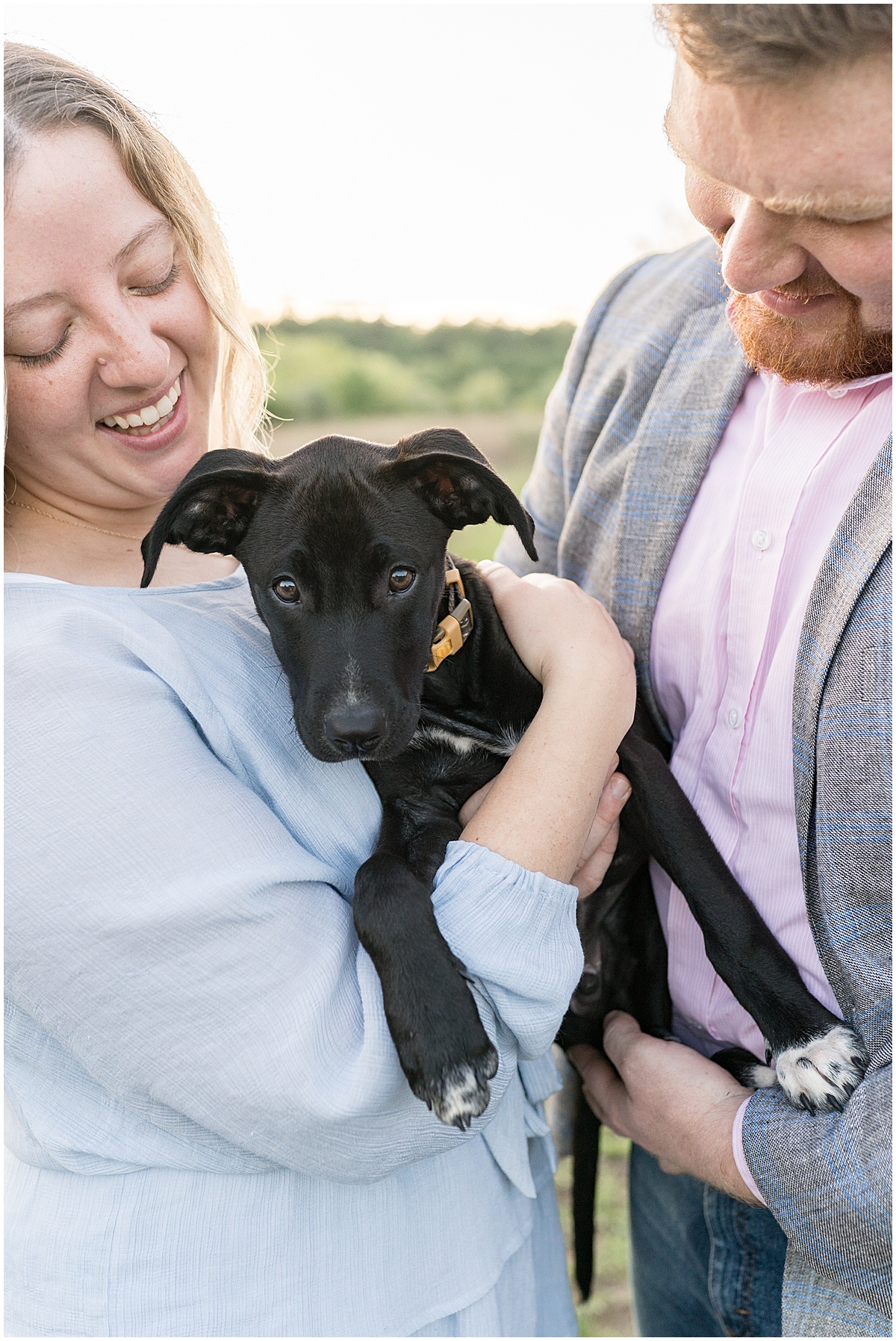 Close up of couple holding black dog during summer engagement photos at Fairfield Lakes Park
