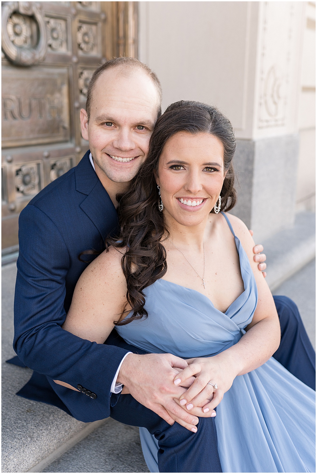 Couple sit by gold doorway at Indiana War Memorial during Downtown Engagement Photos