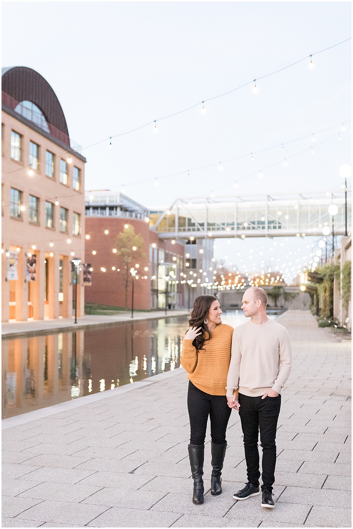 Couple walk under string lights on Indianapolis Canal Walk during Downtown Engagement Photos