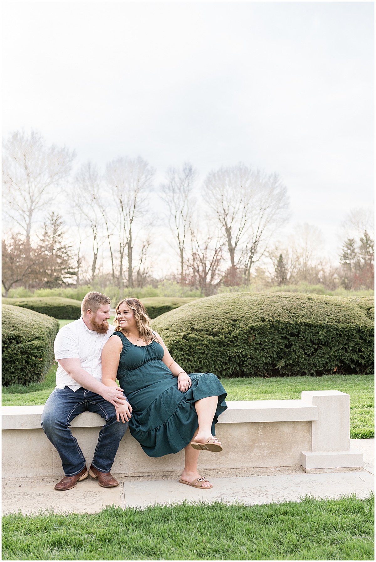 Couple sit on bench at Holcomb Gardens spring engagement photos
