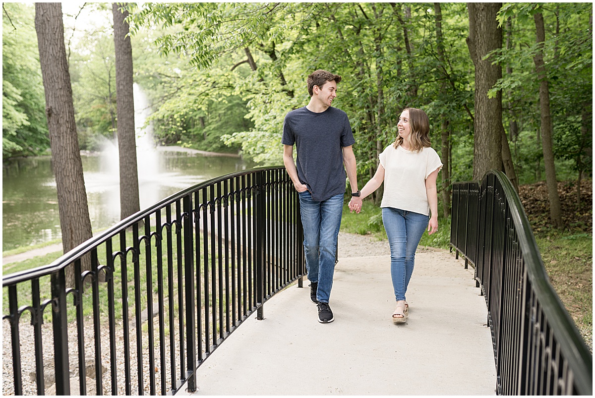 Couple walk over bridge during engagement photos at Holcomb Gardens in Indianapolis.