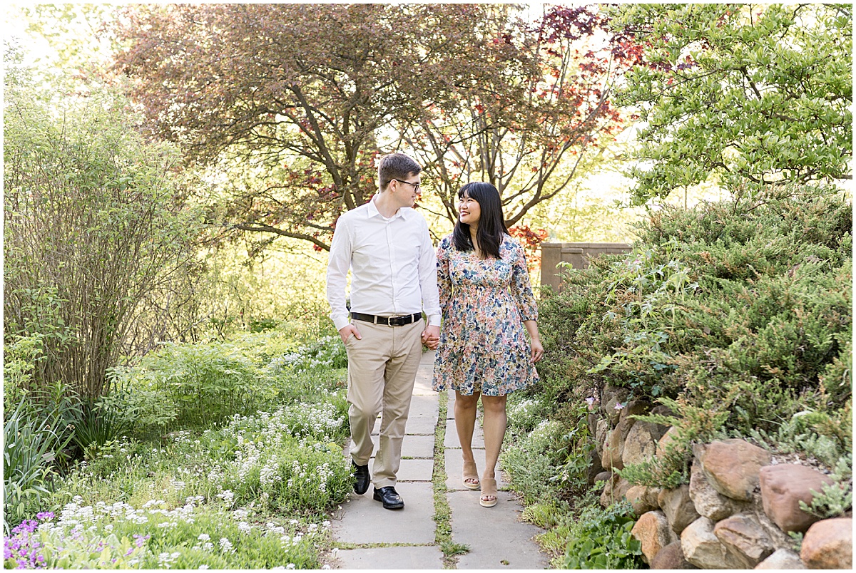 Couple walk through flower garden during engagement photos at Newfields in Indianapolis.
