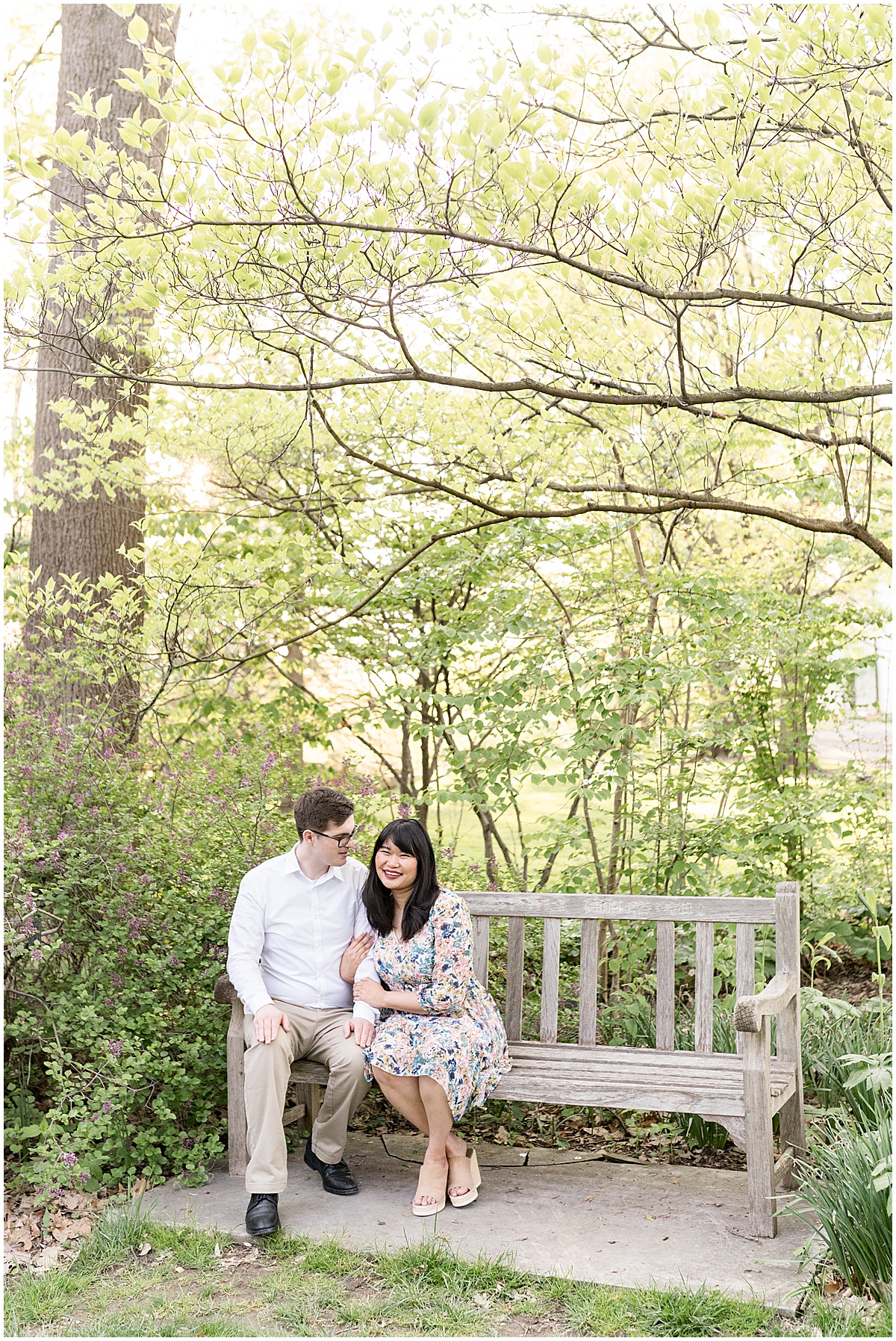 Couple sit on wooden bench during engagement photos at Newfields in Indianapolis.