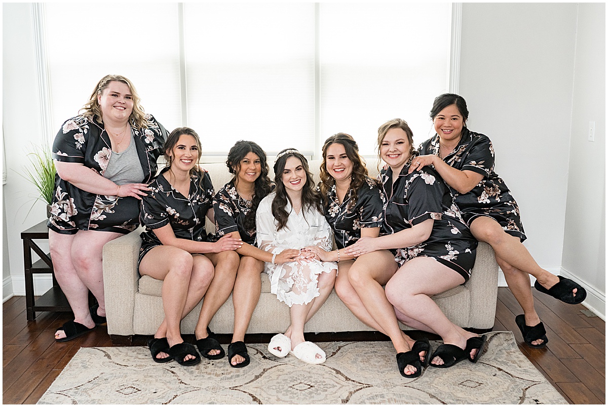 Bride and bridesmaids on couch smiling at camera before Historic Saint Joseph Hall wedding in Indianapolis