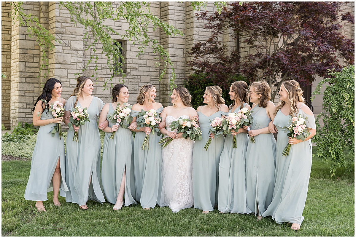 Bridesmaids in sage green walk outside wedding at St. Augustine Catholic Church in Rensselaer, Indiana