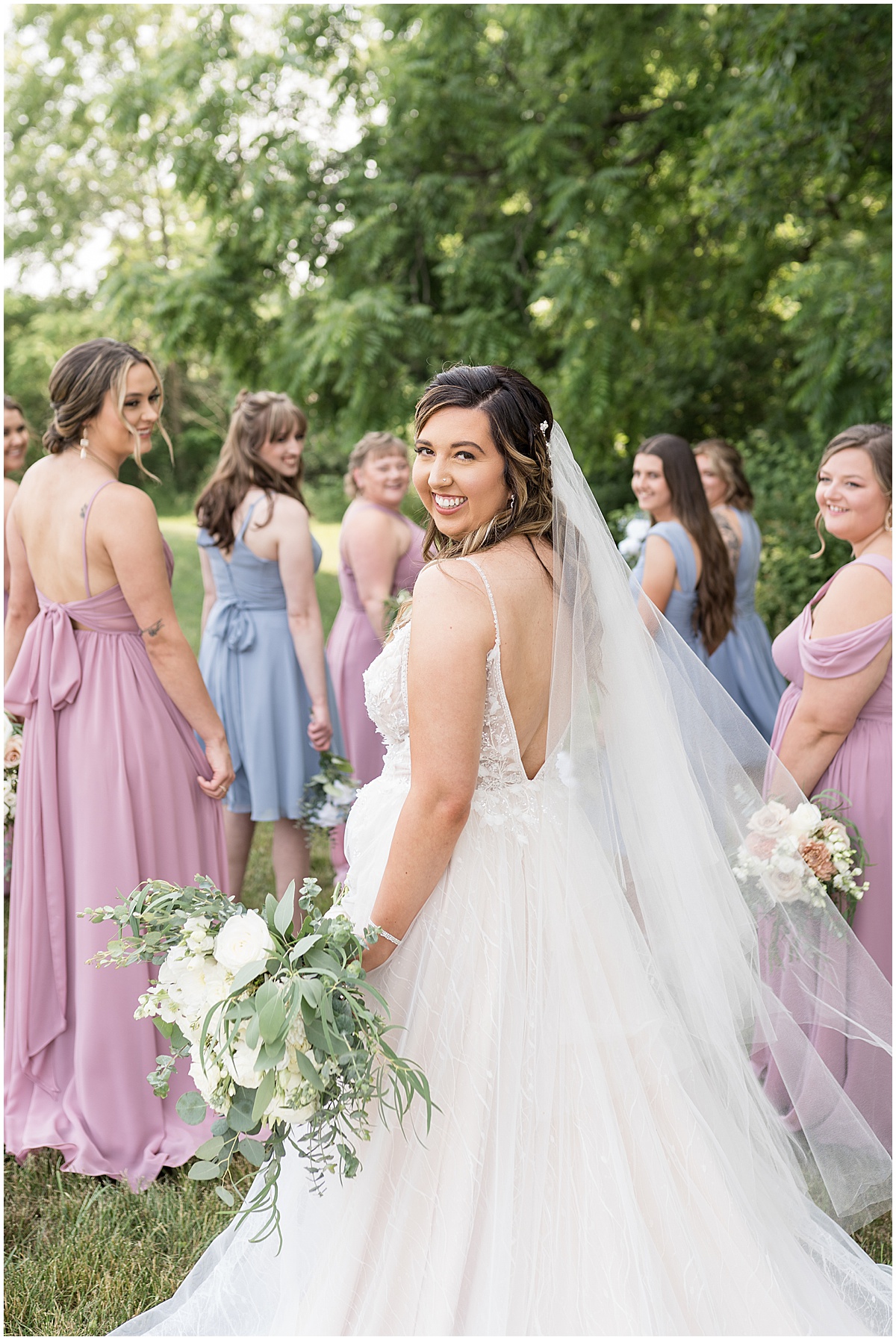 Bride shows back of dress walking with bridesmaids at Stables Event Center wedding in Lafayette, Indiana