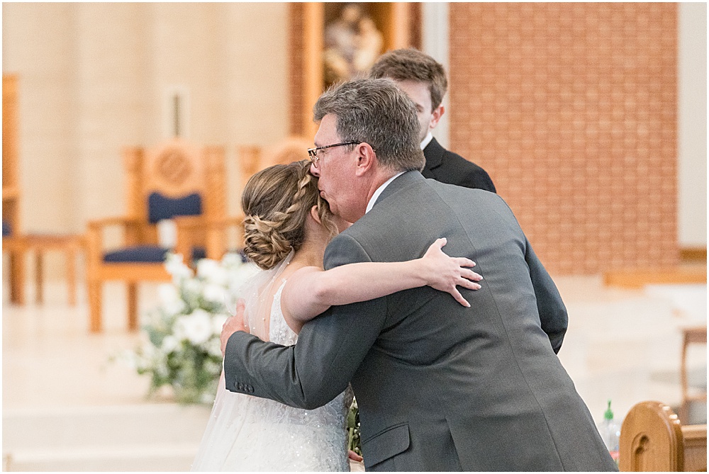 Father kisses bride before giving her to groom during St. Maria Goretti Catholic Church wedding ceremony in Westfield, Indiana