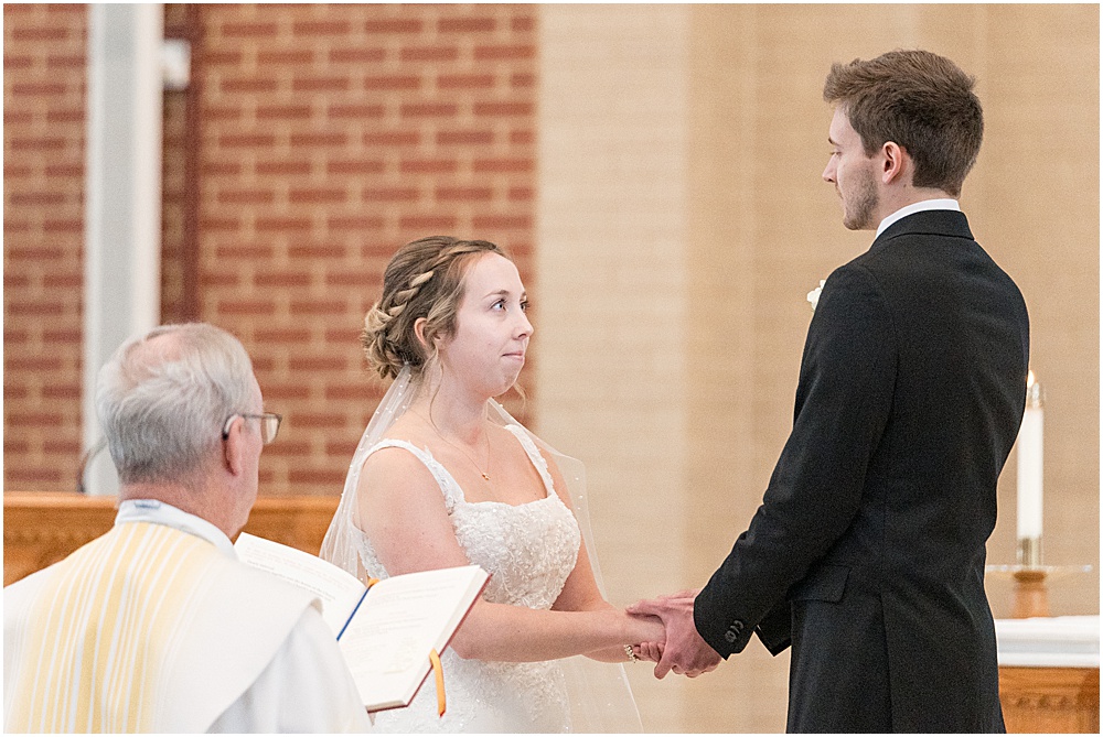 Bride and groom hold hands at altar during St. Maria Goretti Catholic Church wedding ceremony in Westfield, Indiana