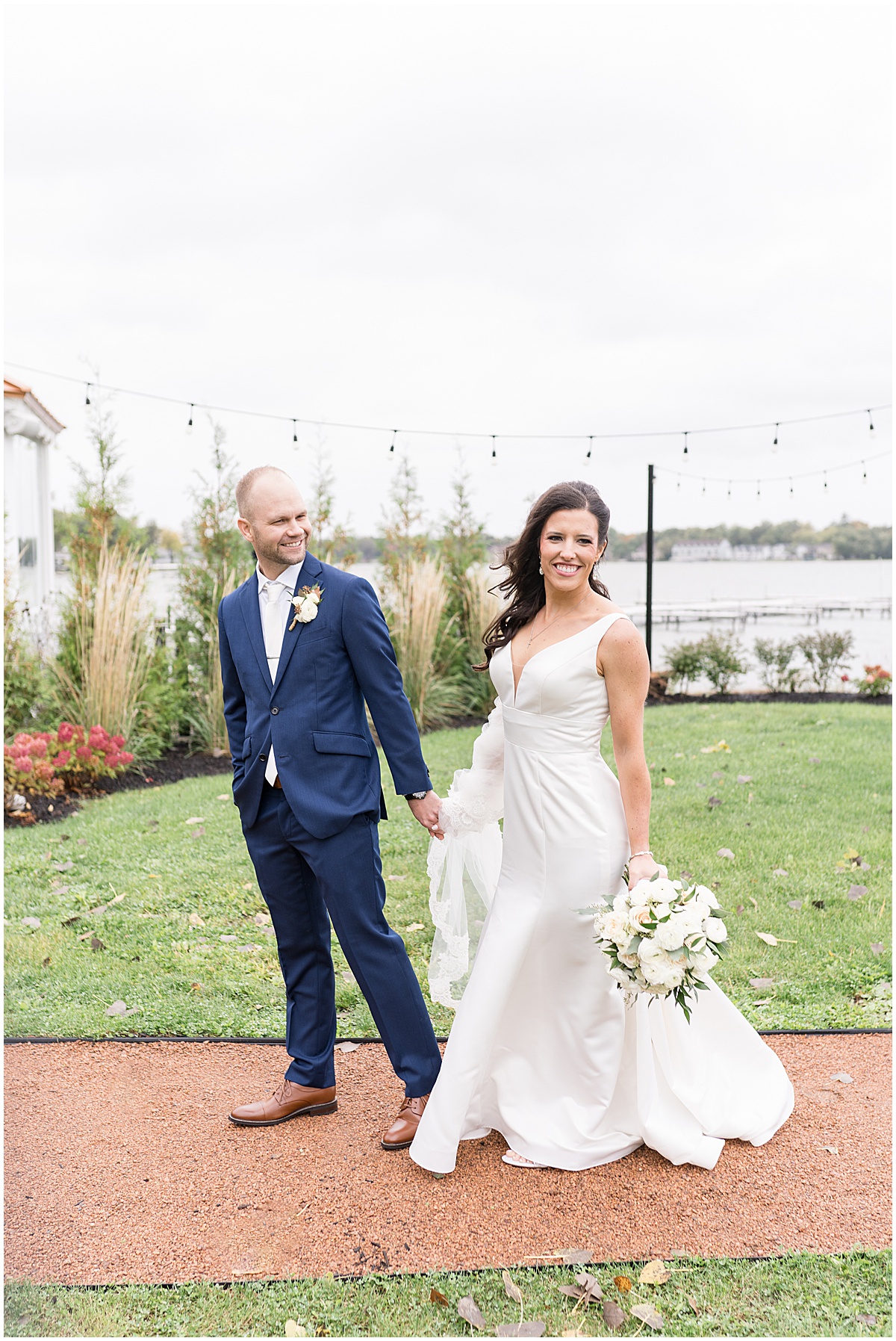 Bride and groom walk by lake at Lighthouse Restaurant wedding in Cedar Lake, Indiana